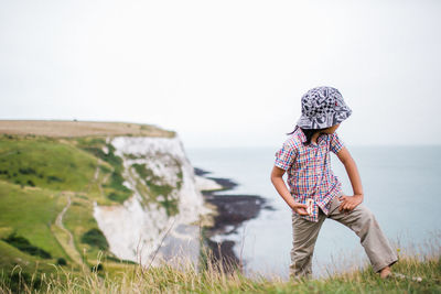 Boy standing on cliff against sky