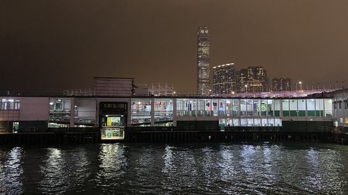 Illuminated buildings by river against sky in city at night