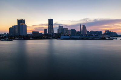 Sea by buildings against sky during sunset