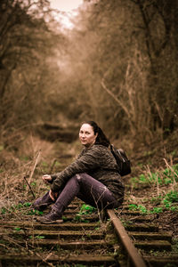 Portrait of young woman in forest sitting on railway 