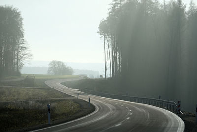 Empty road by trees against sky