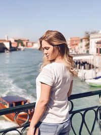 Young woman standing on bridge against canal