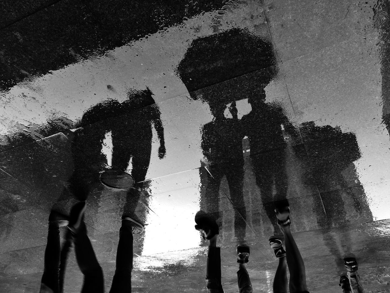 REFLECTION OF PEOPLE ON PUDDLE IN CITY STREET