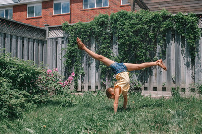 Full length of girl doing handstand against plants in yard