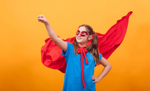 Young woman with arms raised standing against yellow background