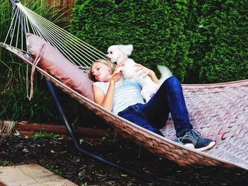 Young woman relaxing with puppy on hammock in yard