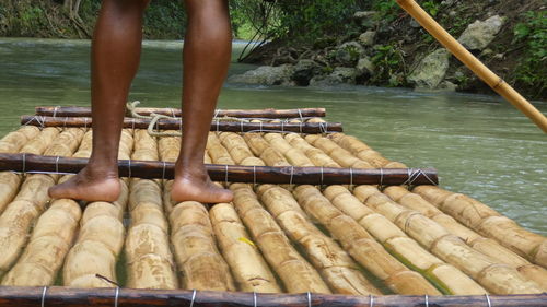 Low section of man standing on wooden raft in river