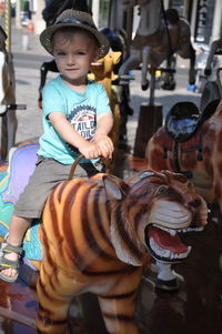 Full length portrait of boy sitting on carousel tiger in amusement park