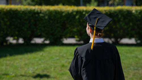 Rear view of woman wearing graduation gown standing on field