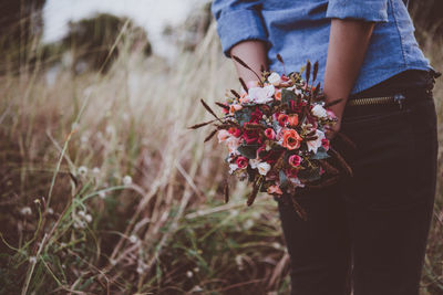 Midsection of woman holding bouquet on field