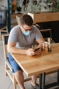 Man wearing mask using mobile phone while sitting at cafe