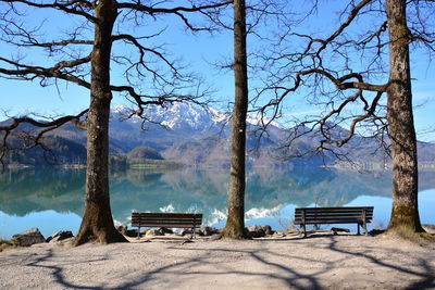 Empty bench by lake against trees and mountain