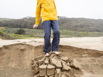 Detail of young person standing on crumbling edge of sandy ledge