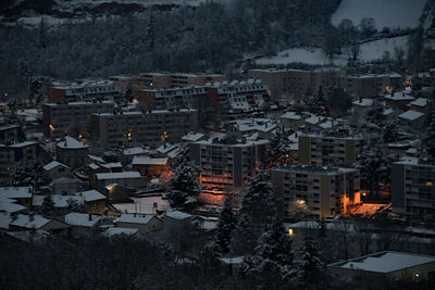 High angle view of illuminated buildings in snowy city at night