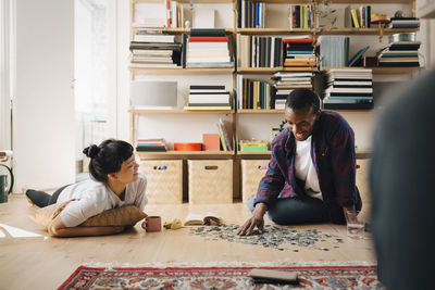 Smiling girlfriend looking at boyfriend solving puzzle in living room at home