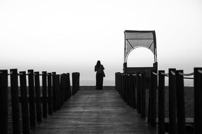 Rear view of woman standing on railing against clear sky