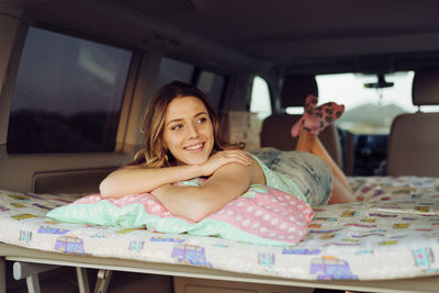 Blonde cheerful pretty woman lying on folding bed inside a minivan and looking away