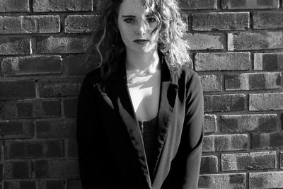 Portrait of young woman standing against brick wall