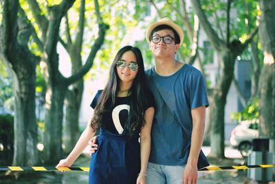 Portrait of smiling young woman wearing sunglasses standing against trees