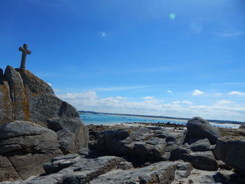 Low angle view of cross on rock at beach against cloudy sky