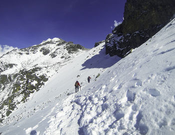 Rear view of people hiking on snowcapped mountains against sky