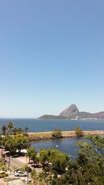 Scenic view of sea and mountains against clear blue sky