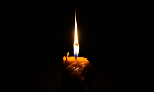Close-up of hand holding lit candle in darkroom