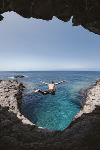 Full length of man jumping from cliff at sea