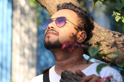 Man wearing sunglasses looking up by tree