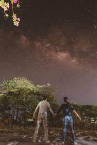 Rear view of man standing by tree against sky at night