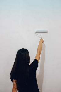 Rear view of woman painting wall with paint roller