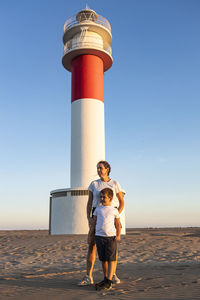 Full length of mother and son standing against lighthouse