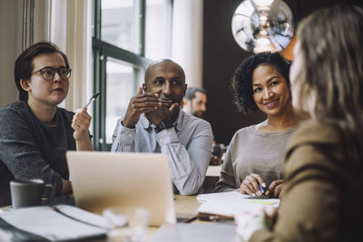 Smiling male and female colleagues looking at businesswoman discussing plan at desk in creative office