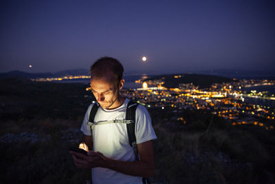 Man looking at illuminated cityscape against sky at night