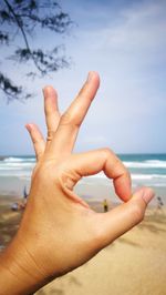 Cropped hand of person gesturing ok sign against beach