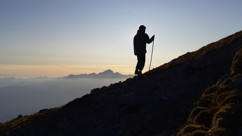 Silhouette boy standing on mountain against sky during sunset