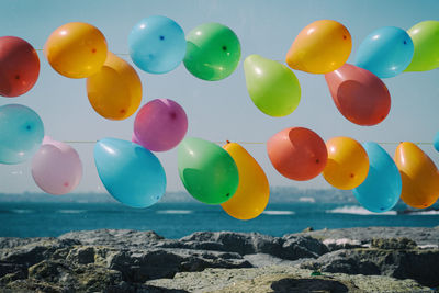 Multi colored balloons on rocks by sea against sky