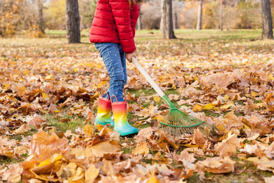 Low section of kid standing with broom by trees during autumn