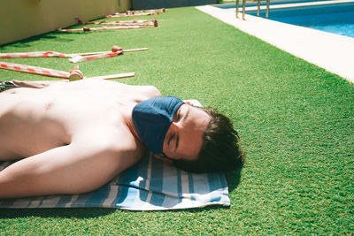 Shirtless man lying on grass by swimming pool