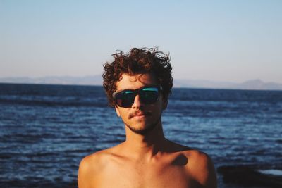 Portrait of young man wearing sunglasses at beach against sky