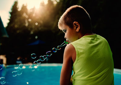 Rear view of boy blowing bubbles at poolside