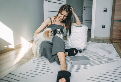Woman tenderly holding two japanese chin dogs, on the floor affection and pet care at home