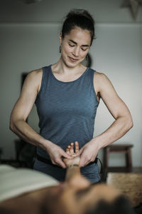 A fit female massage therapist smiles while treating a patient