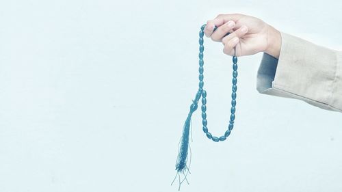 Close-up of hand holding rope against white background