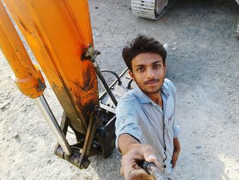 High angle portrait of man holding monopod while standing by machinery on field