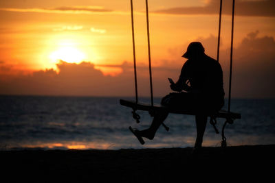 Silhouette man sitting on beach against sky during sunset