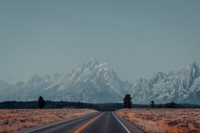 Road by snowcapped mountains against sky during winter