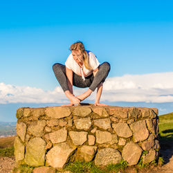 Young woman doing yoga against blue sky