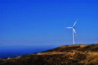 Wind turbines on land by sea against clear blue sky