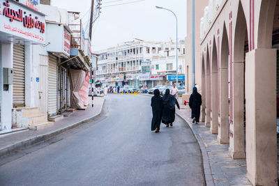 Rear view of people walking on road amidst buildings